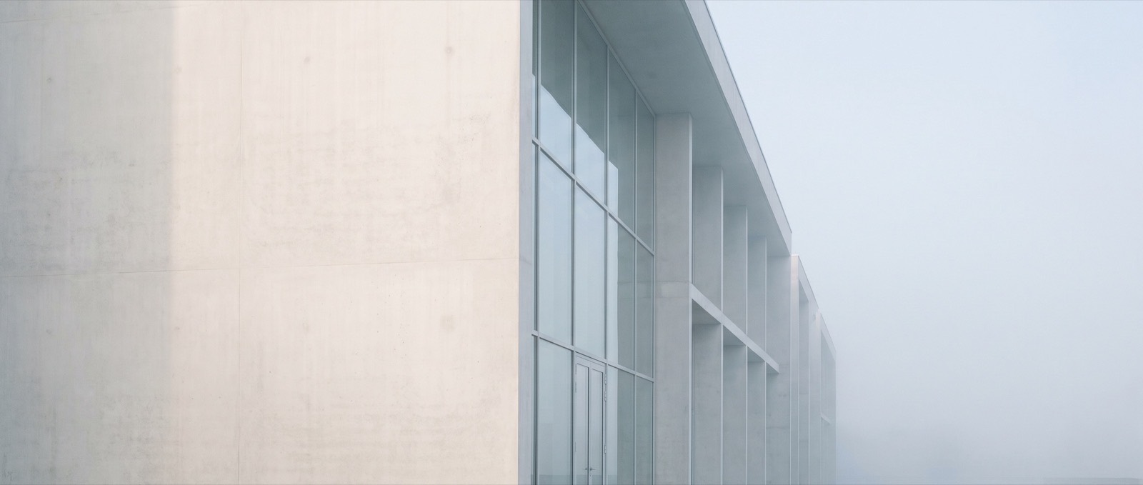 A pale concrete and glass facade receding into soft morning haze, its window bays repeating in even rhythm.